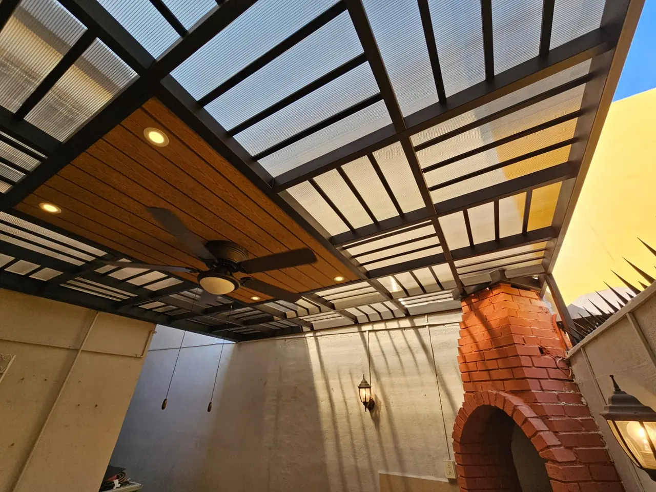 Techo de policarbonato y deck sintético con ventilador sobre un patio con asador de ladrillo