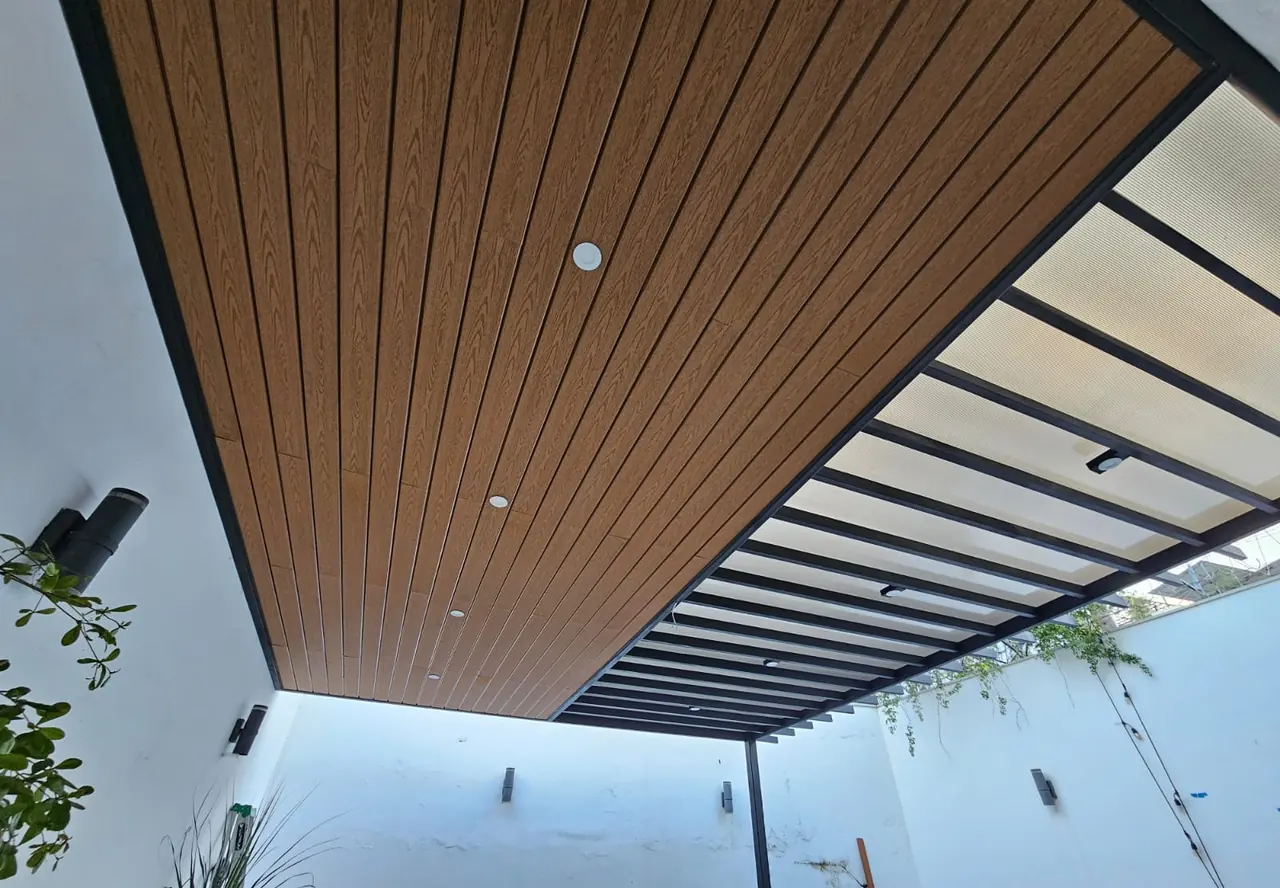 Techo de deck sintético con spots y franja de policarbonato sobre un patio con jardín