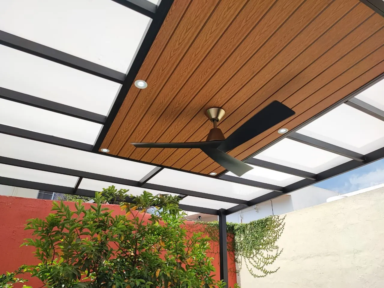 Techo de policarbonato y deck sintético con ventilador sobre un patio con árboles