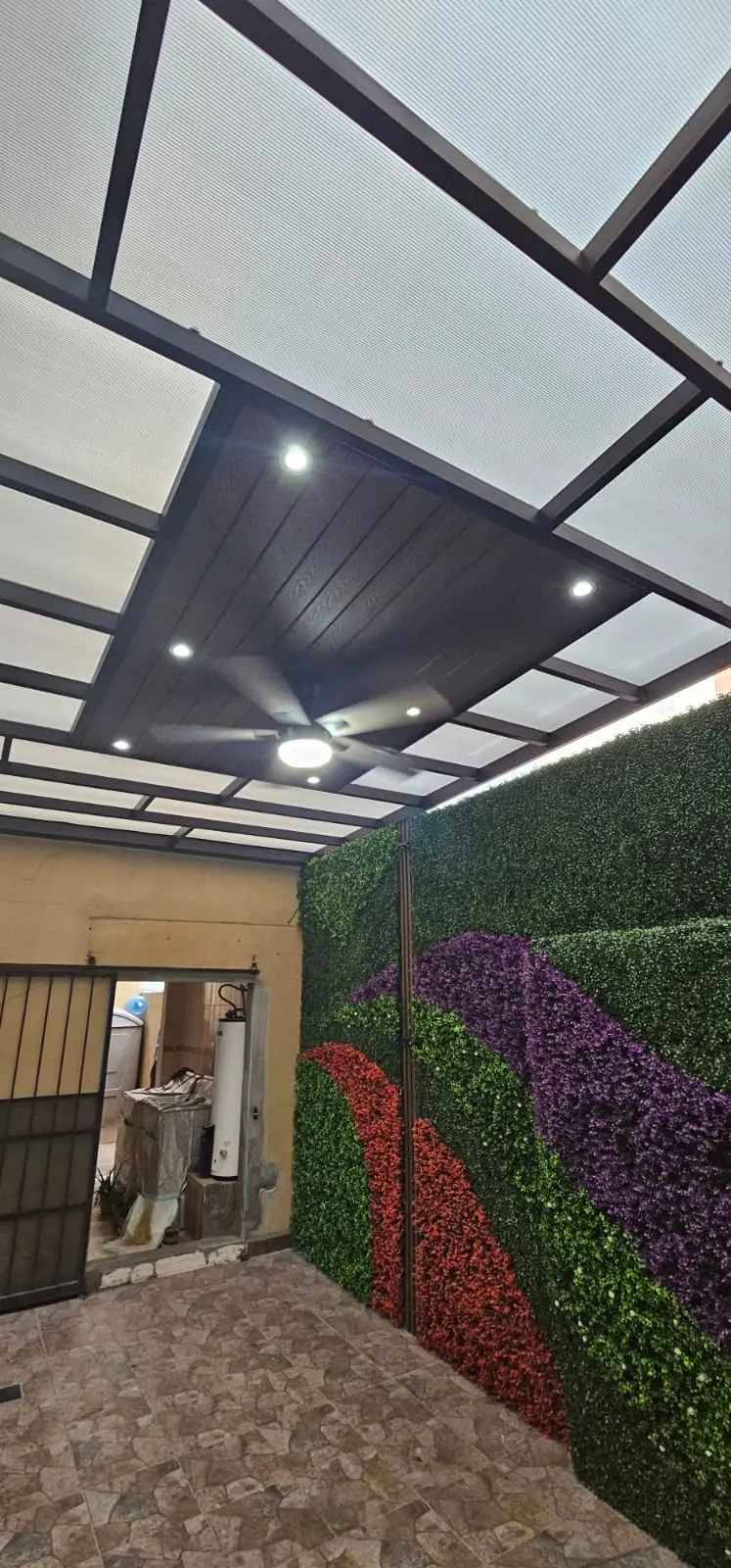 Techo de policarbonato y deck sintético con ventilador sobre un patio con muro verde