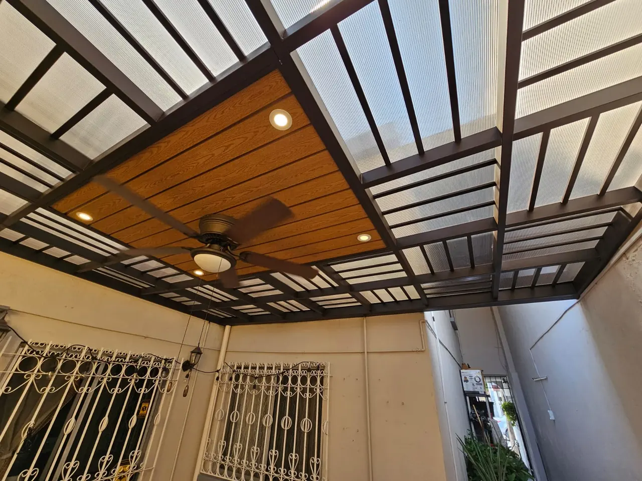 Cubierta combinada de policarbonato y deck sintético con spots y ventilador de techo sobre un patio