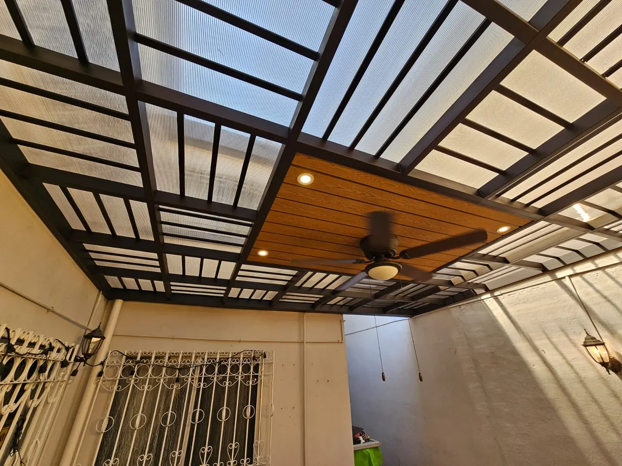 Estructura metálica oscura con policarbonato y deck sintético vista desde un extremo del patio